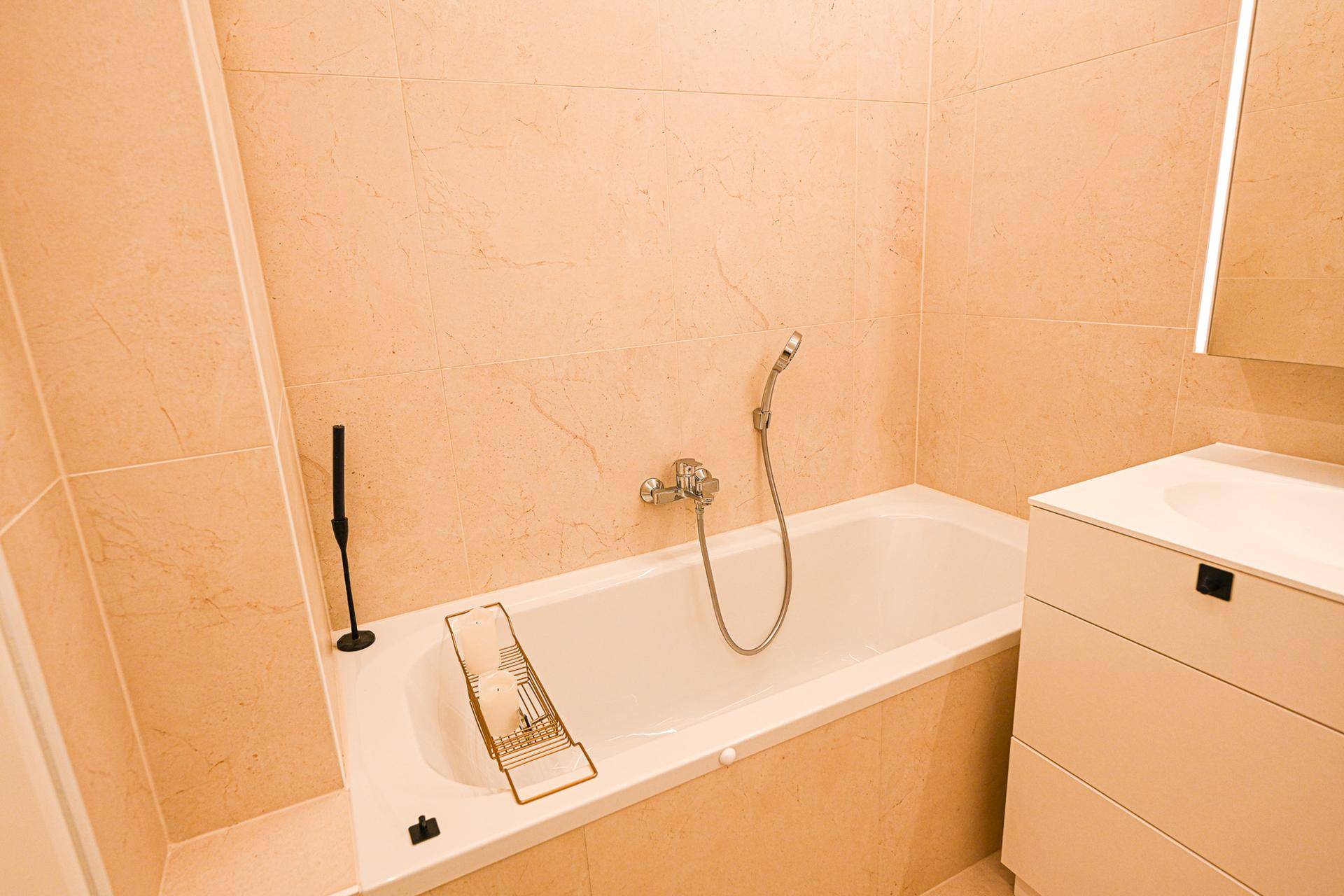 Eingebaute Badewanne mit beigefarbenen Fliesen und Duscharmatur.