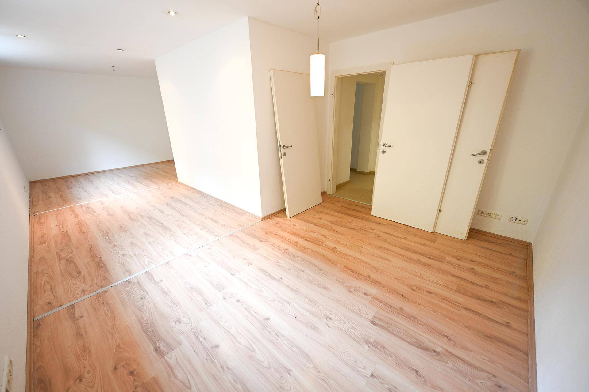 Geräumiger Raum mit hellem Laminatboden und mehreren Türen.