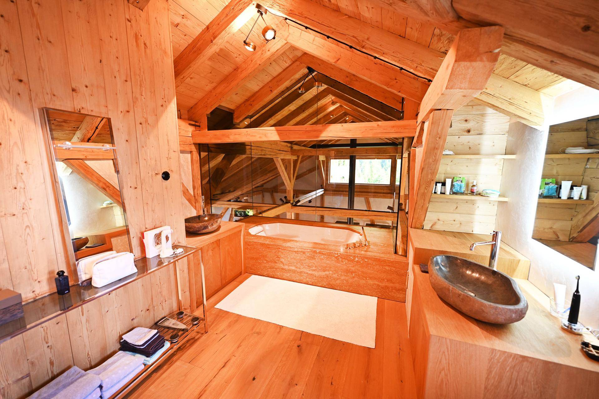 Luxuriöses Badezimmer mit eingebauter Badewanne, zwei Aufsatzwaschbecken und offener Holzkonstruktion.