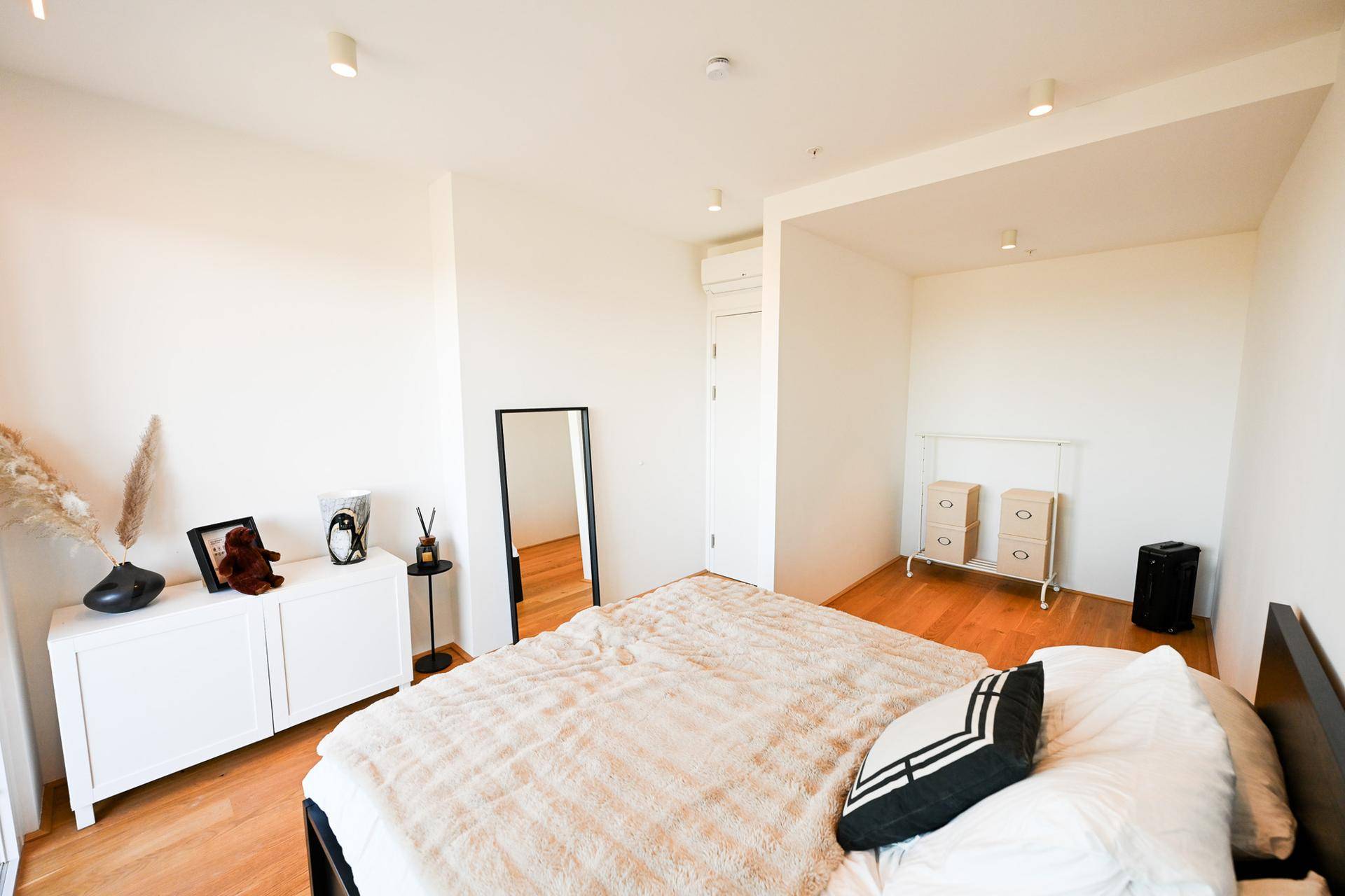 Helles Schlafzimmer mit Holzboden, minimalistischer Einrichtung und viel Tageslicht.