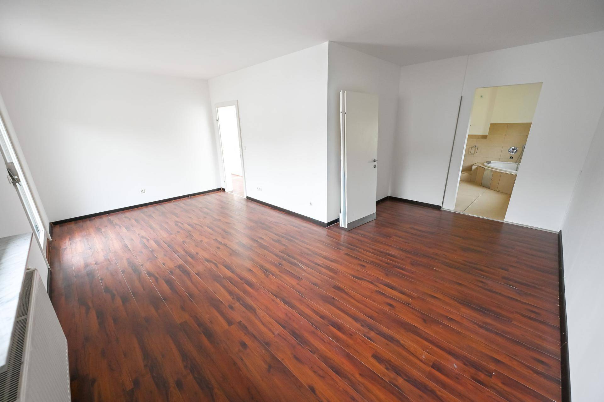 Geräumiges Zimmer mit dunklem Laminatboden und weiß gestrichenen Wänden.