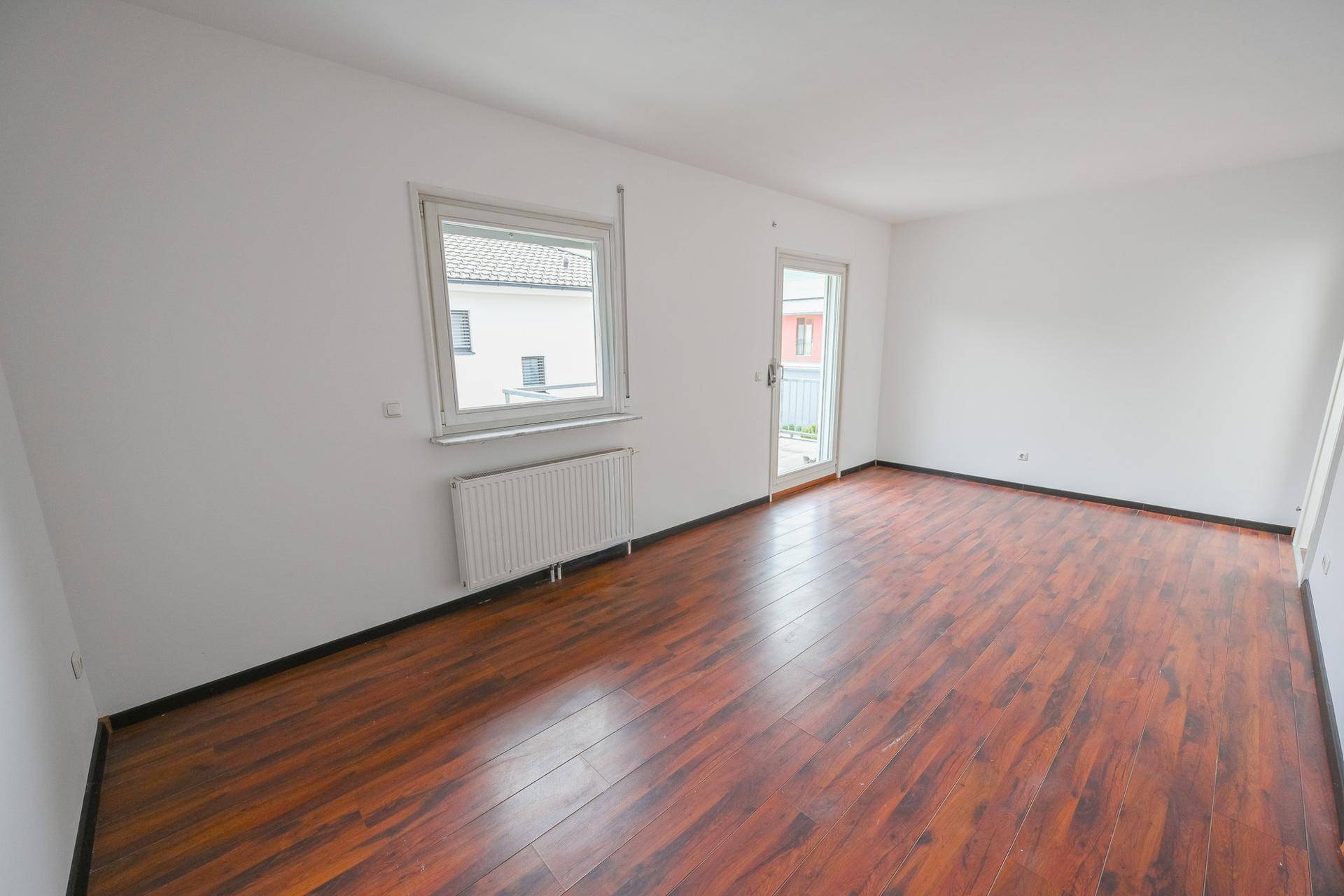 Helles Zimmer mit Laminatboden, Heizkörper und Zugang zum Balkon.