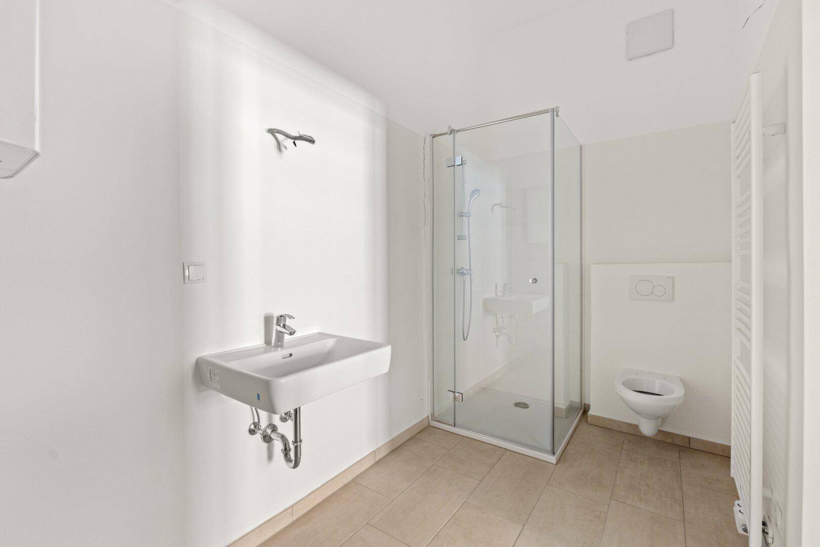 Modernes Badezimmer mit ebenerdiger Dusche, wandhängendem WC und hellem Fliesenboden.