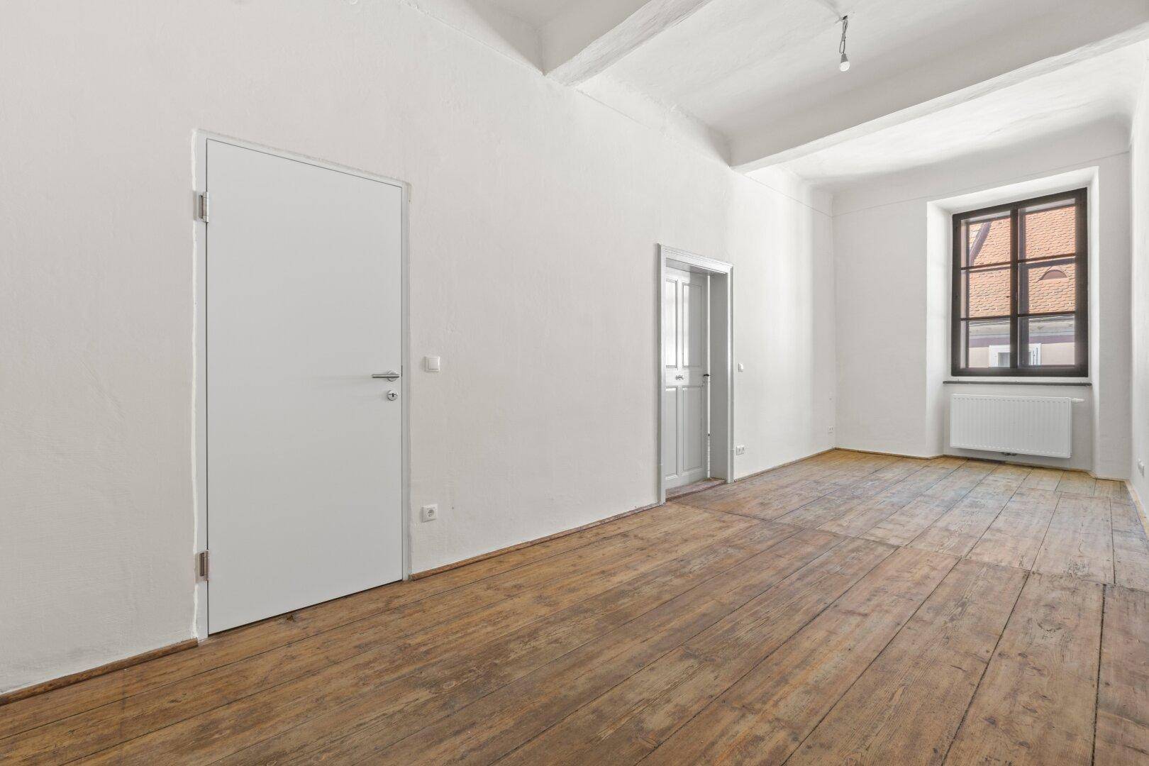 Heller Raum mit originalem Holzdielenboden, weißen Wänden und sichtbaren Deckenbalken.