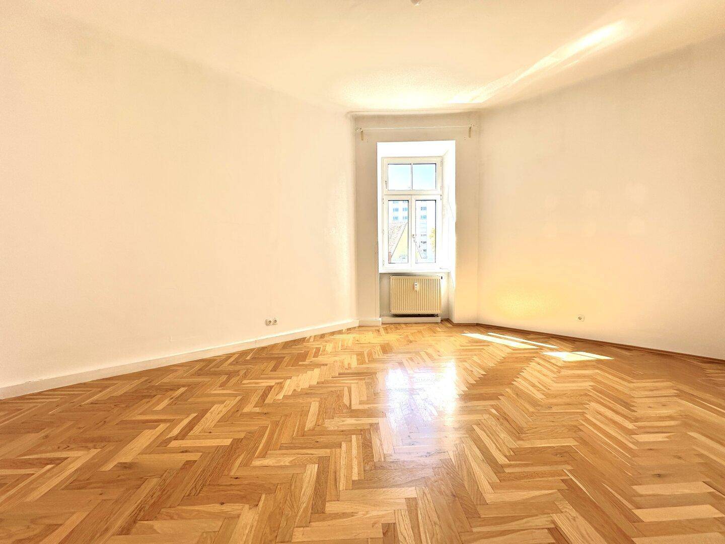 Geräumiges, helles Zimmer mit klassischem Fischgrätparkett und hohen Decken, ideal für Wohnzwecke.
