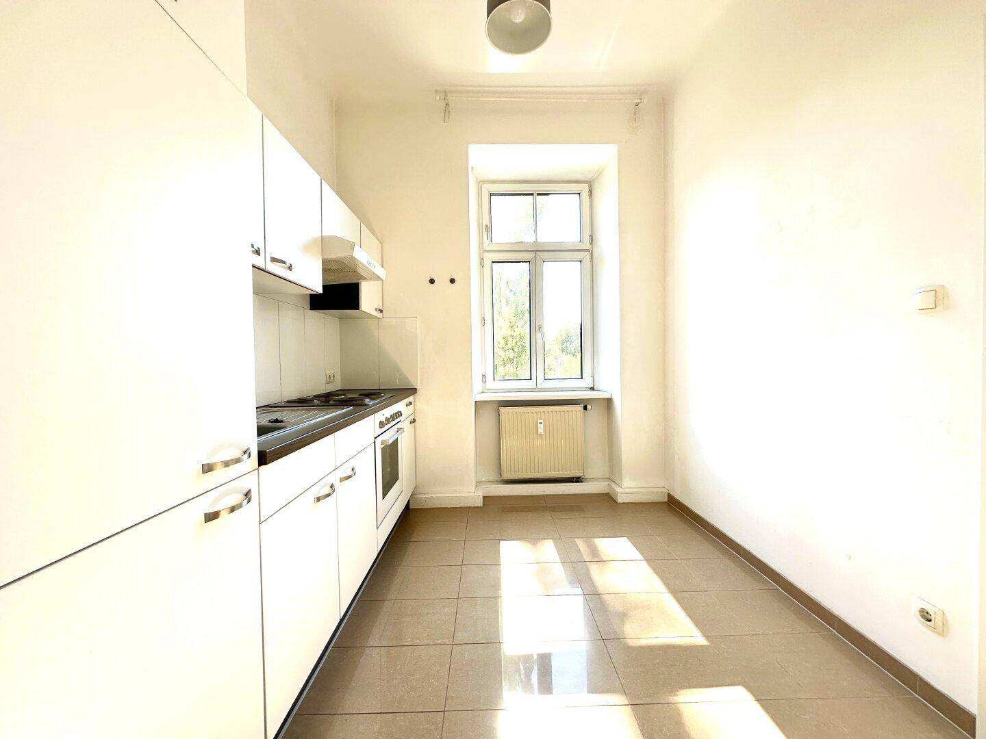 Funktionale Küche mit weißen Einbauschränken, Fliesenboden und einem Fenster für natürliches Licht.