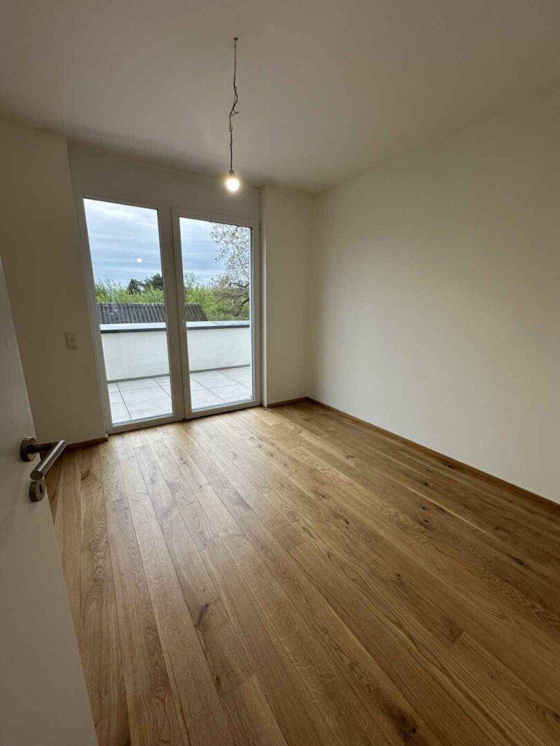 Helles Zimmer mit Holzparkett und direktem Zugang zu einer Außenterrasse.