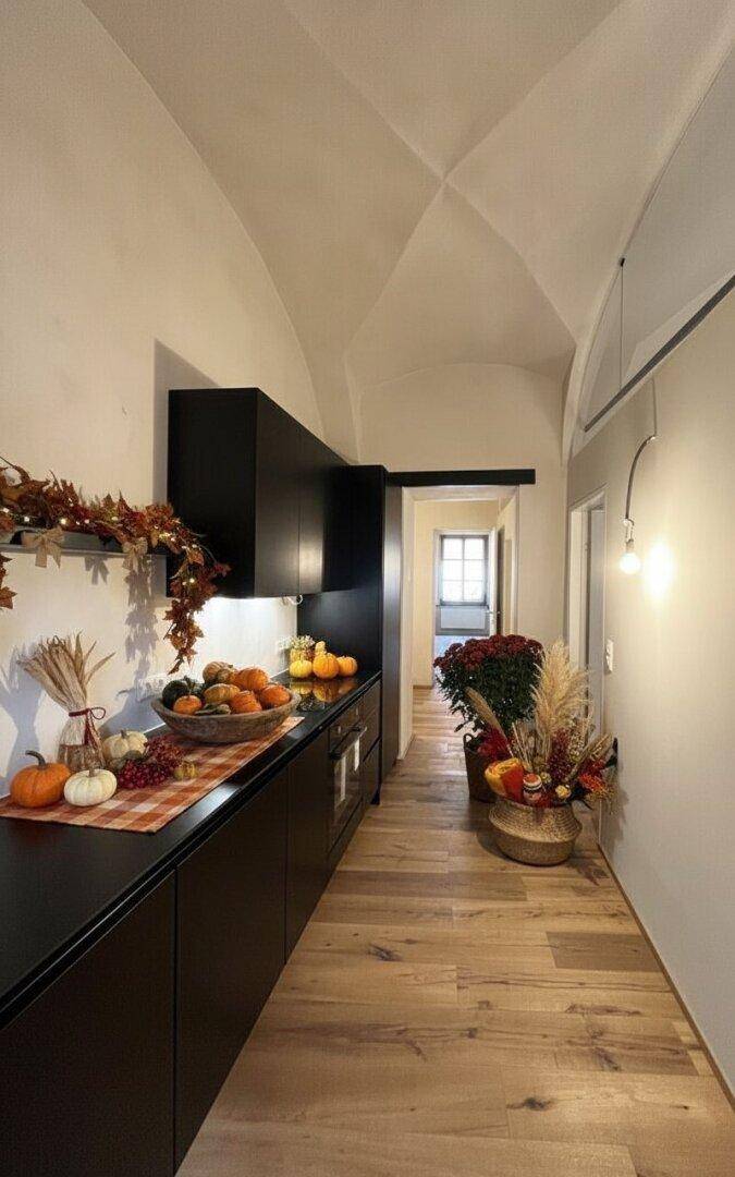 Schlanke, moderne Küche mit schwarzen Schränken, Holzboden und gewölbter Decke.