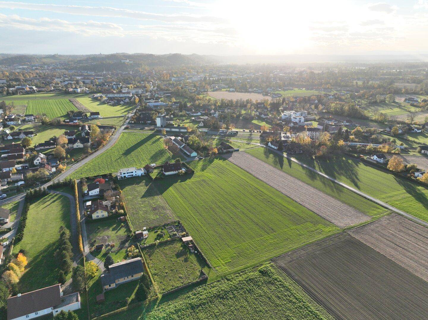 Umfassende Luftaufnahme einer ländlichen Gegend mit Wohnsiedlungen und landwirtschaftlichen Flächen unter hellem Himmel.