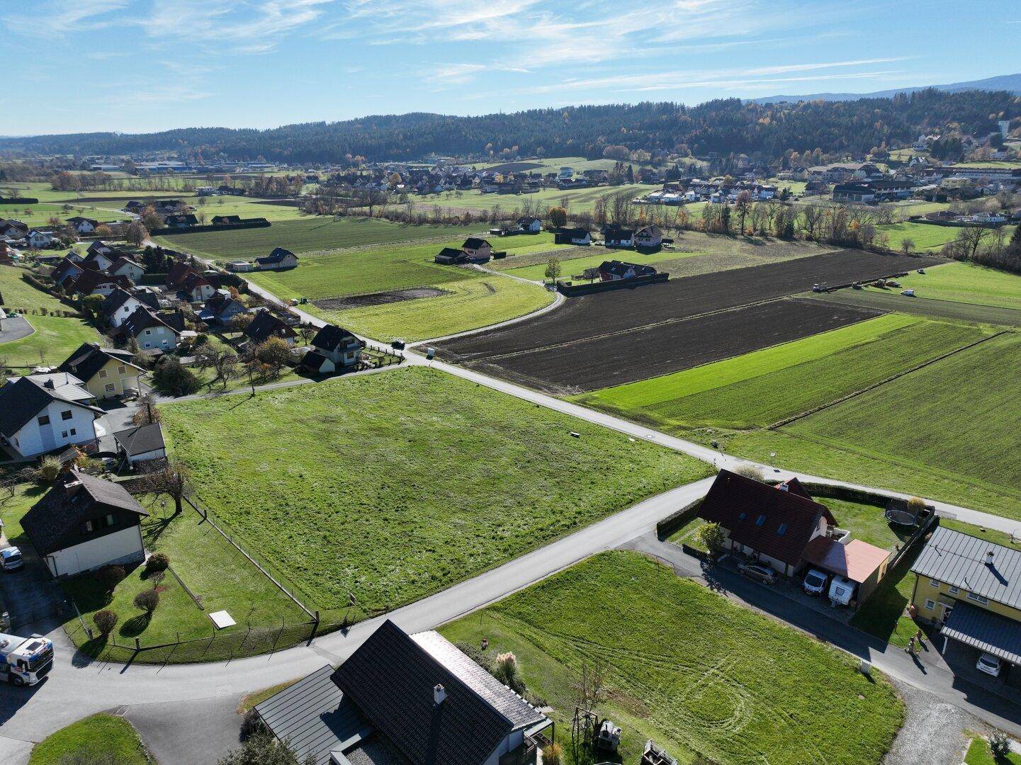 Weitläufige Luftaufnahme mit Blick auf grüne Felder, Wohnhäuser und die umliegende Landschaft.