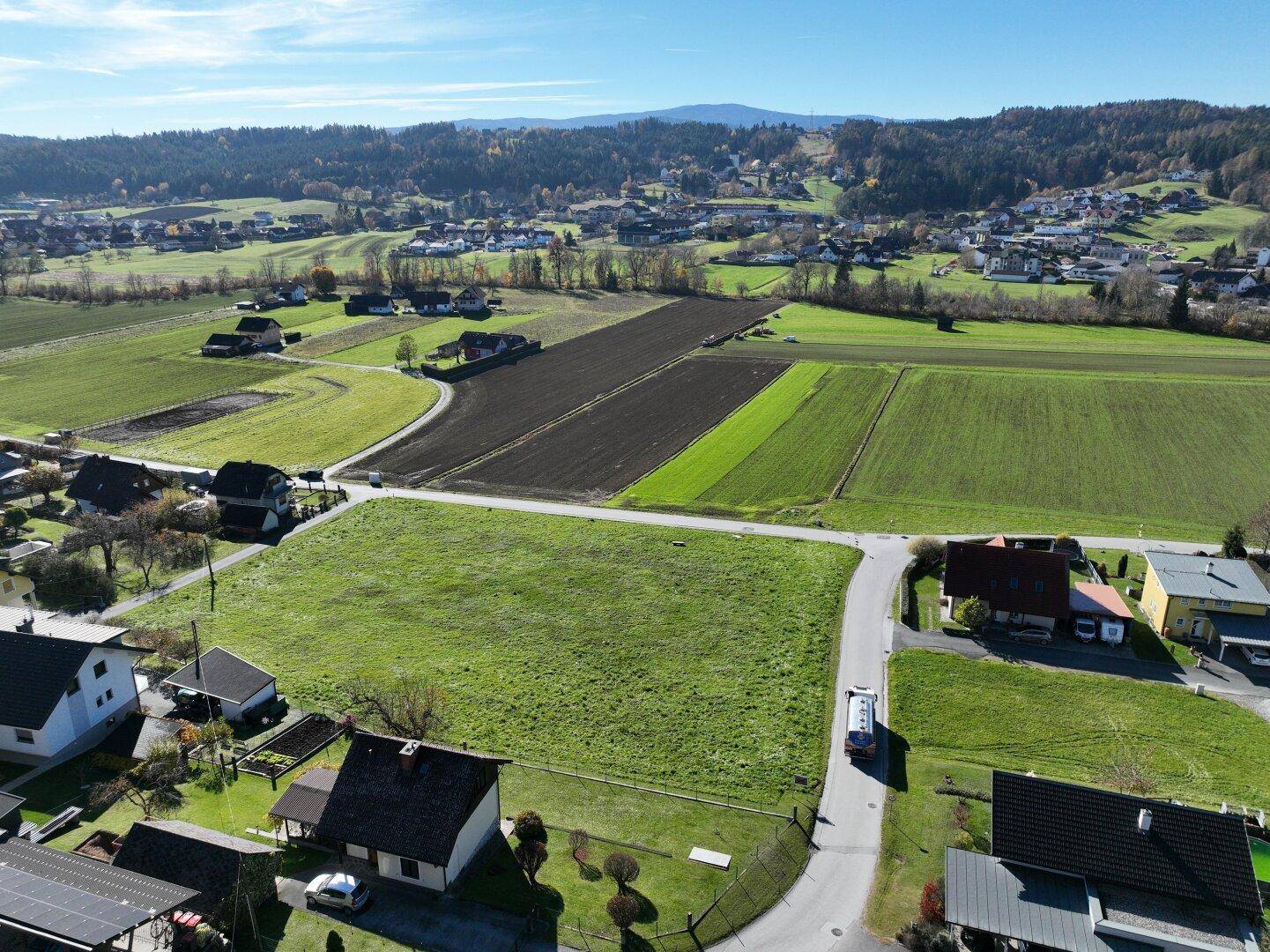 Weitläufige Luftaufnahme eines grünen Baugrundstücks, umgeben von Feldern und einer ländlichen Siedlung.