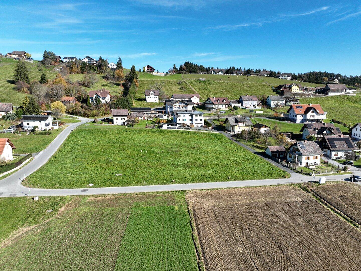 Weitläufiges grünes Grundstück aus der Vogelperspektive, eingebettet in eine ländliche Wohnsiedlung unter blauem Himmel.