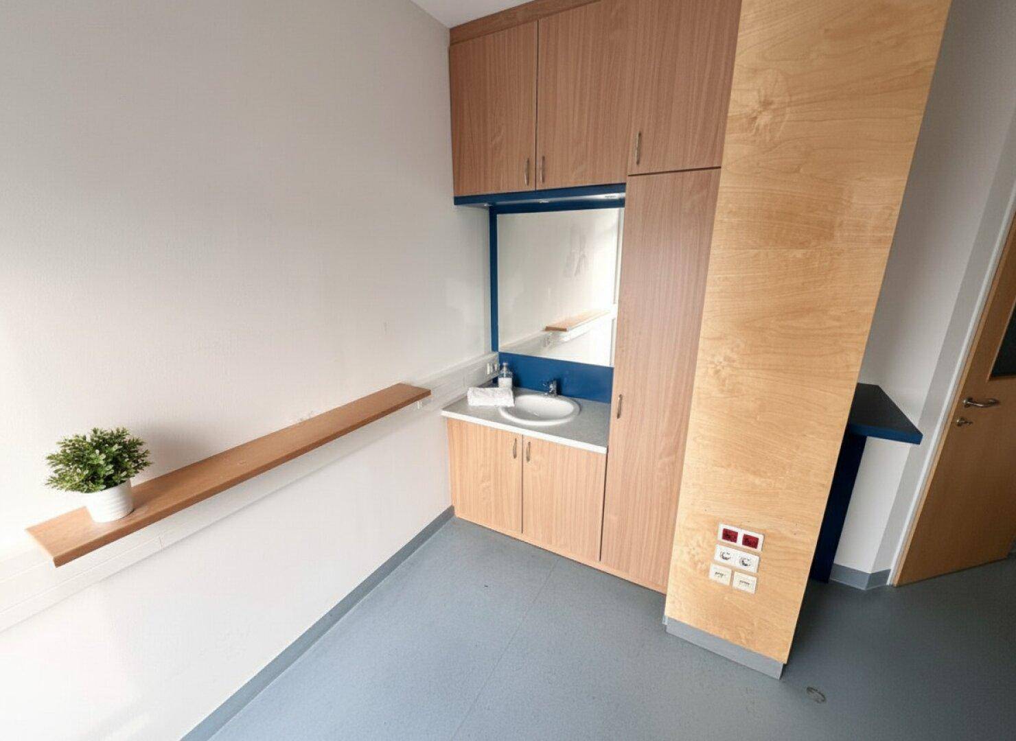 Funktionaler Raum mit Waschbecken, Spiegel und Holzschränken, ideal für eine Praxis oder ein Büro.
