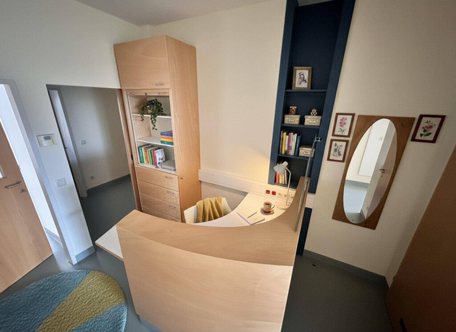 Kleiner Bürobereich mit einem geschwungenen Holzschreibtisch, integrierten Regalen und einem Spiegel.