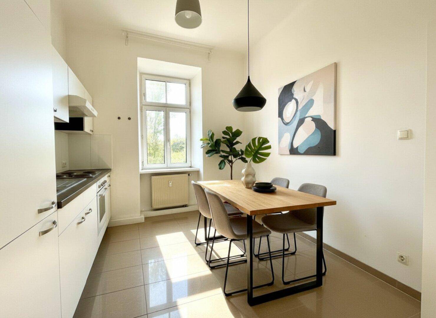 Moderne Küche mit weißen Schränken, Fliesenboden und Essbereich am Fenster.