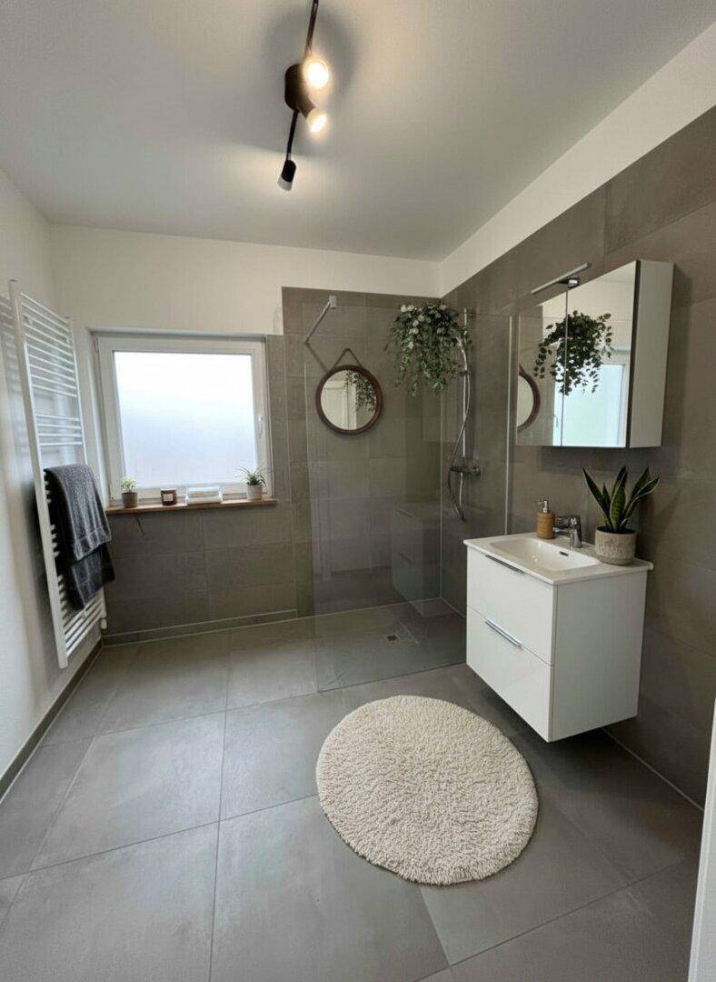 Modernes Badezimmer mit begehbarer Dusche, grauen Fliesen und Fenster für Tageslicht.