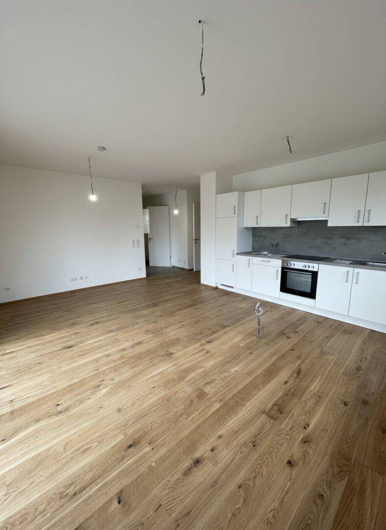 Geräumiger, unmöblierter Wohnbereich mit offener Küchenzeile und hochwertigem Holzboden.