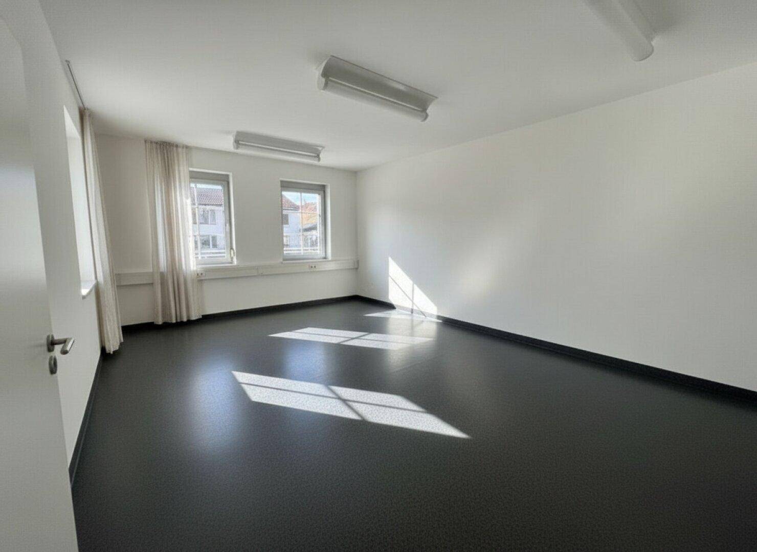 Leerer, heller Büroraum mit großen Fenstern und dunklem Bodenbelag, bereit zur individuellen Einrichtung.