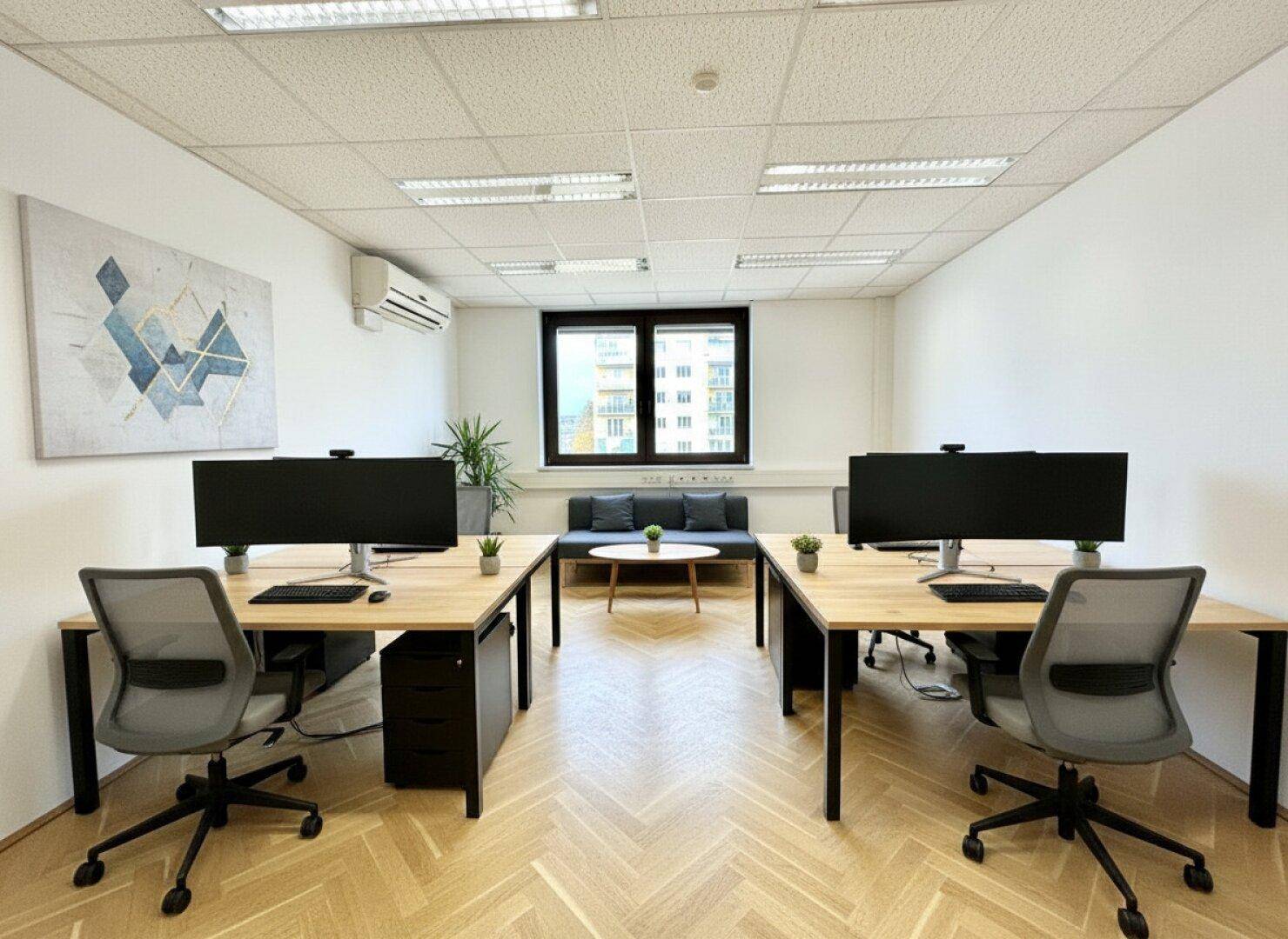 Offener Bürobereich mit zwei Arbeitsplätzen, Monitoren und einer kleinen Sitzecke mit Sofa.