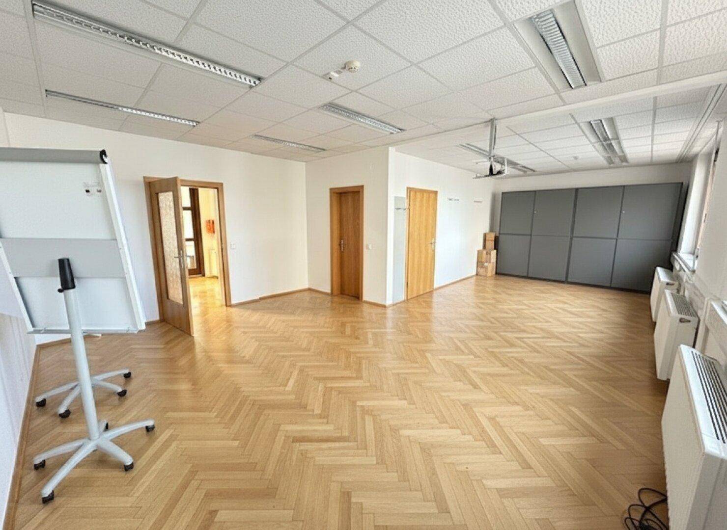 Geräumiger, leerer Konferenzraum mit Fischgrätparkettboden und Holztüren, bereit zur Einrichtung.