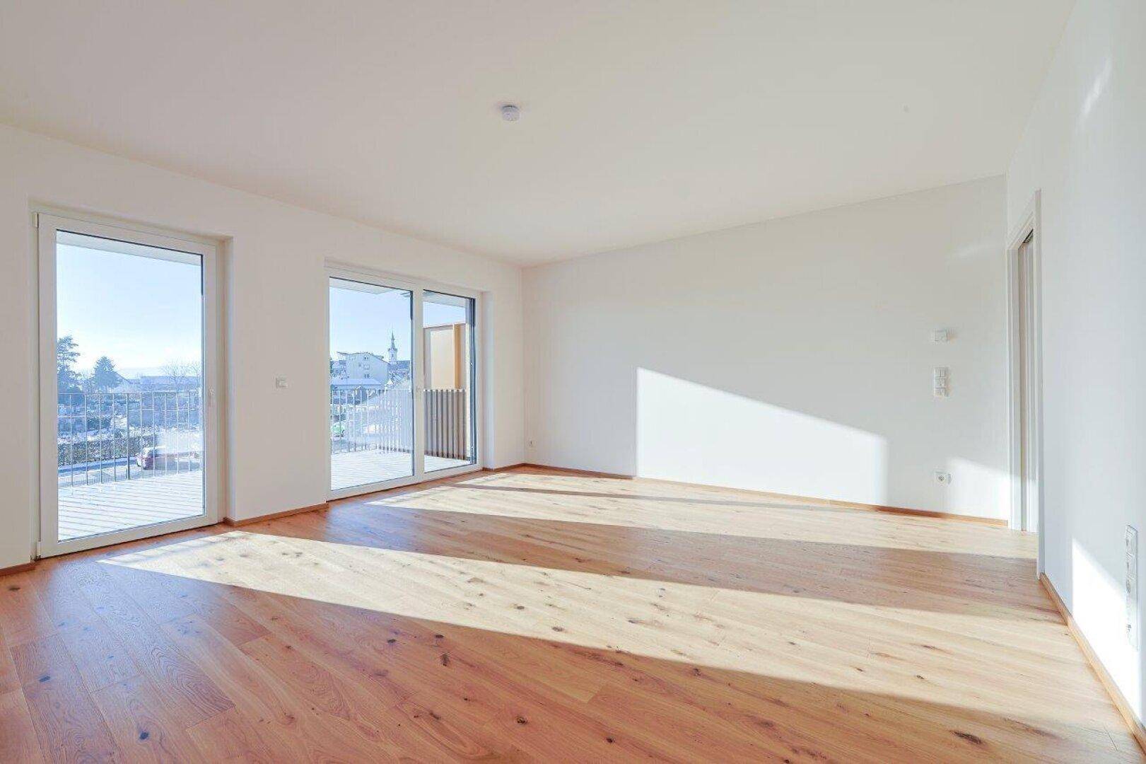 Lichtdurchflutetes Wohnzimmer mit Holzboden und großen Schiebetüren, die auf einen Balkon führen.
