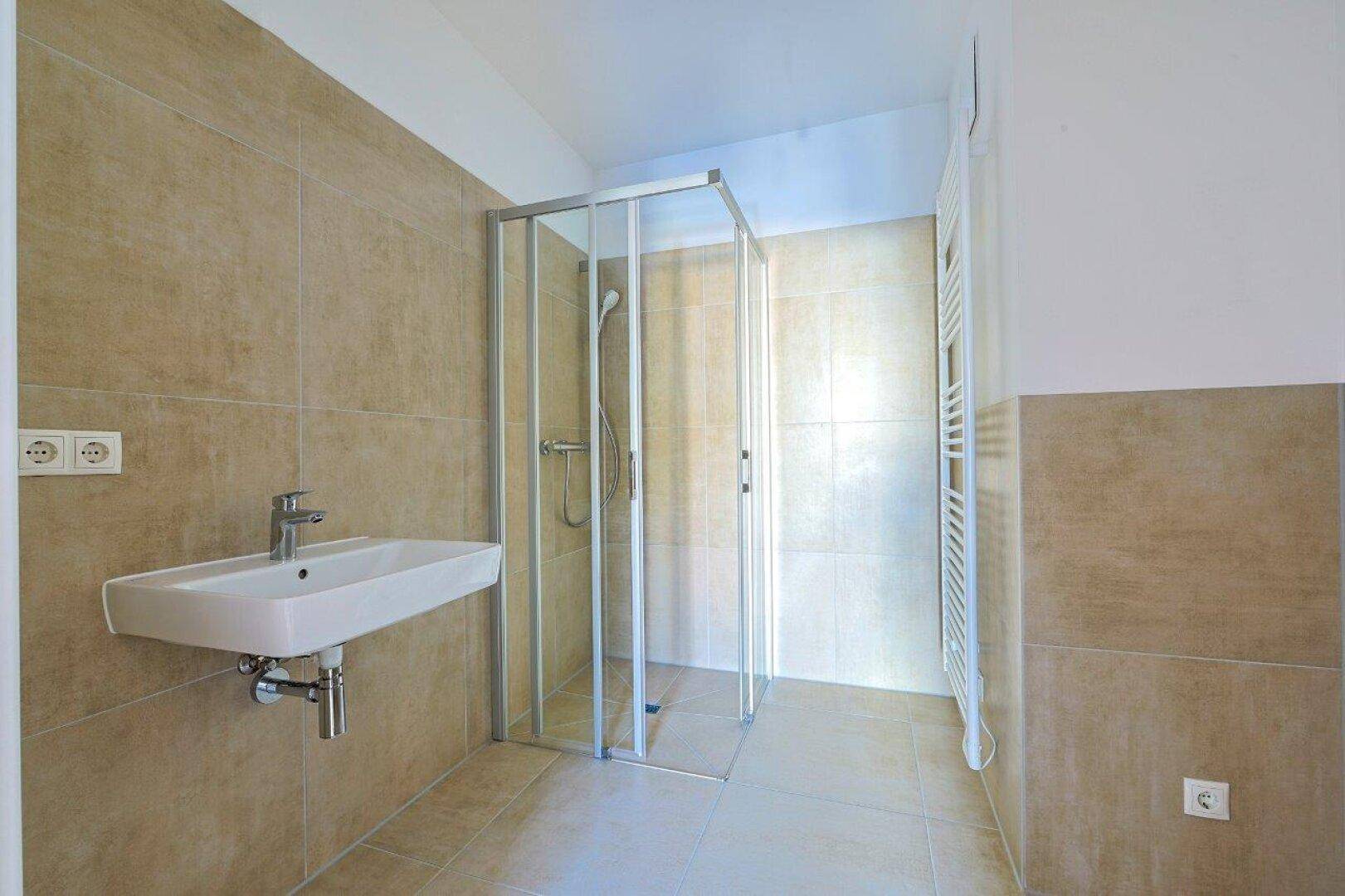 Modernes Badezimmer mit beigefarbenen Fliesen, Duschkabine, Waschbecken und Handtuchheizkörper.