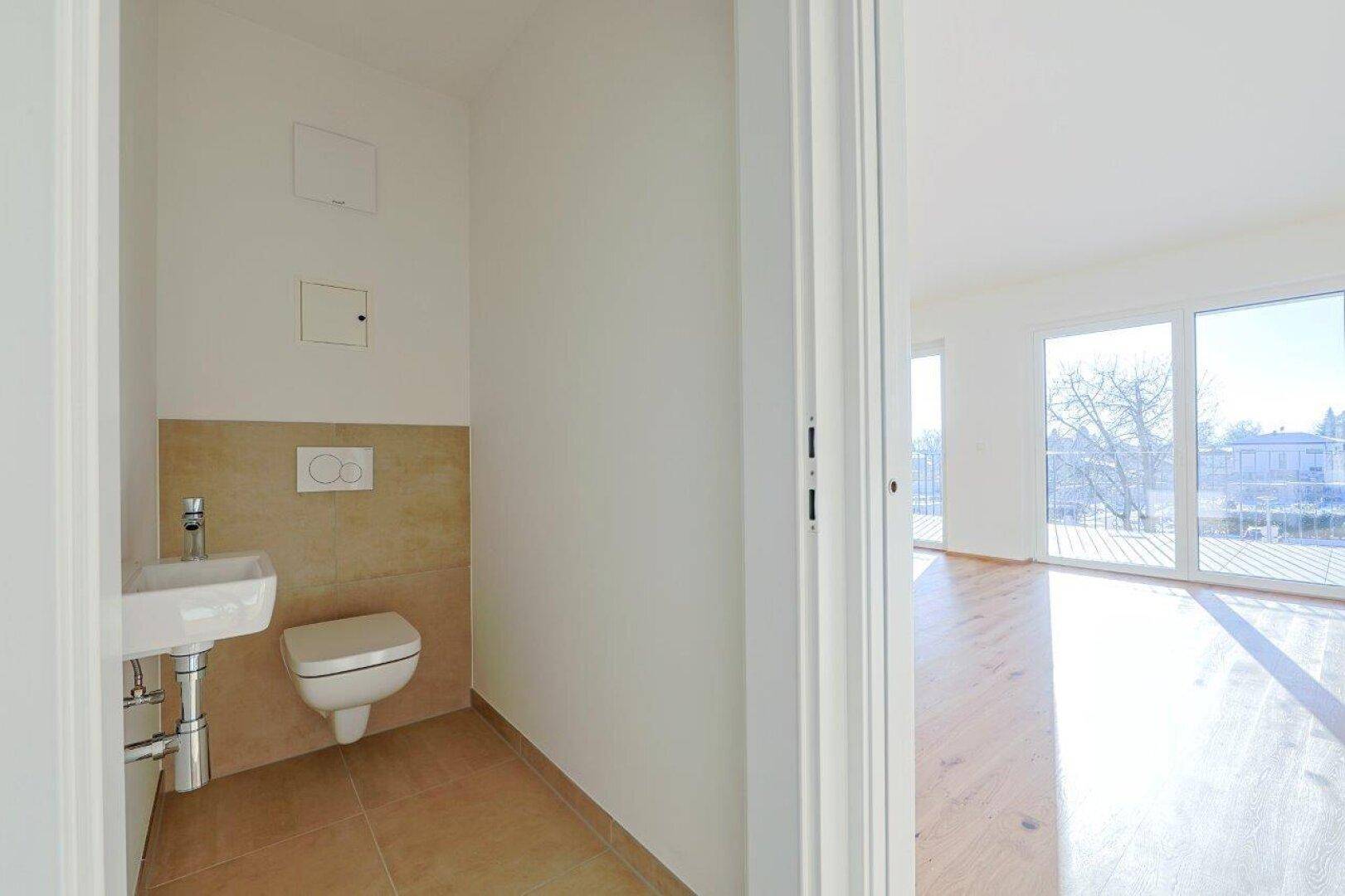 Modernes Gäste-WC mit wandhängender Toilette, kleinem Waschbecken und beigefarbenen Fliesen.