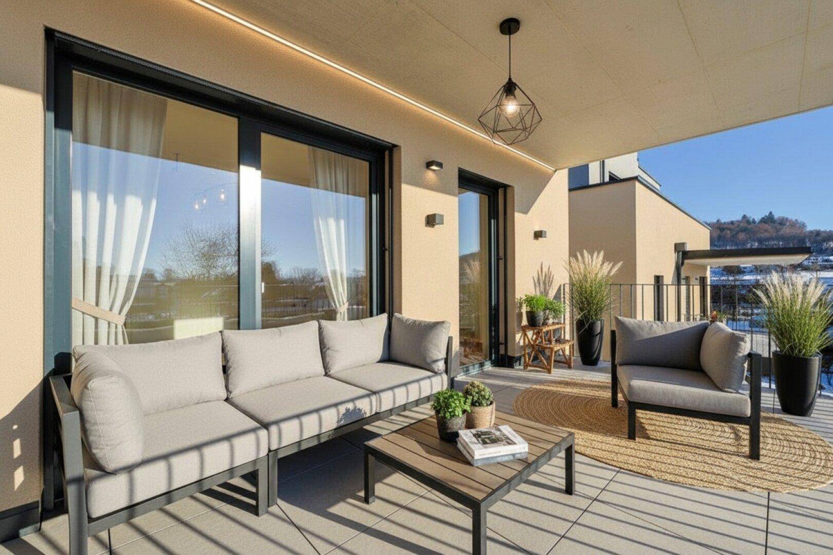 Möblierte Sonnenterrasse mit Lounge-Möbeln, Pflanzen und Blick auf die Umgebung.