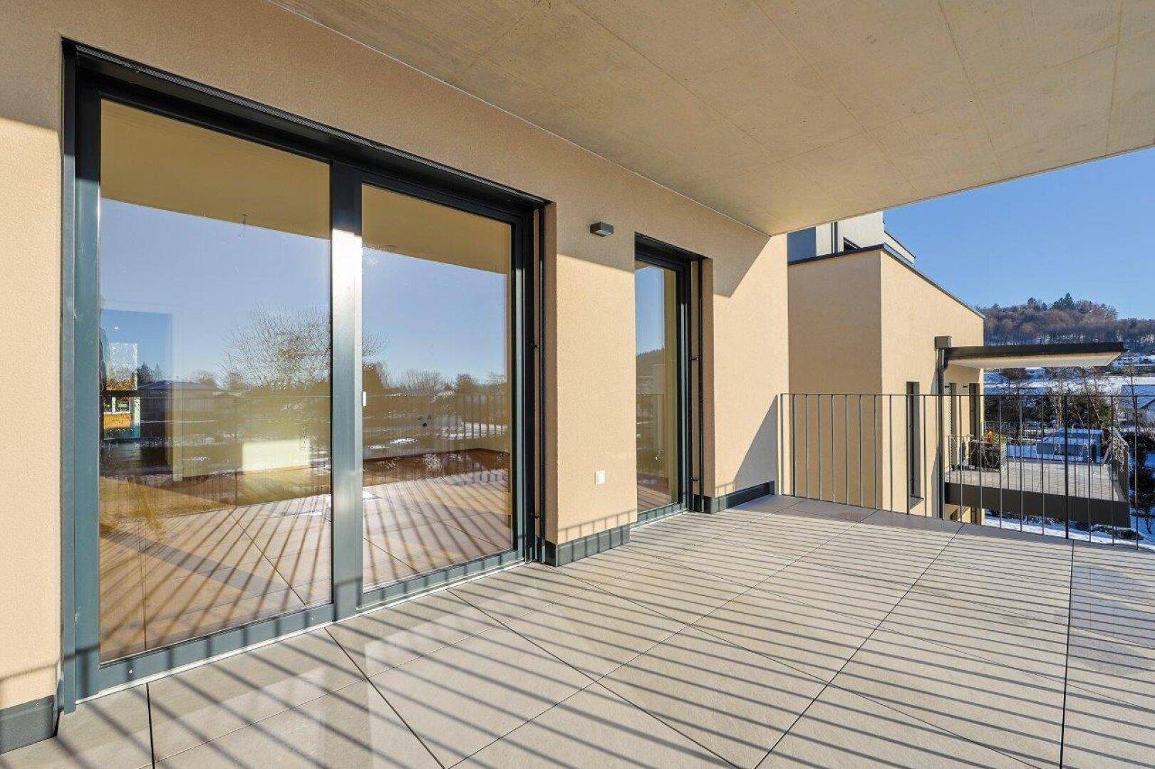 Geräumige, leere Terrasse mit Fliesenboden und Blick auf die umliegende Landschaft.