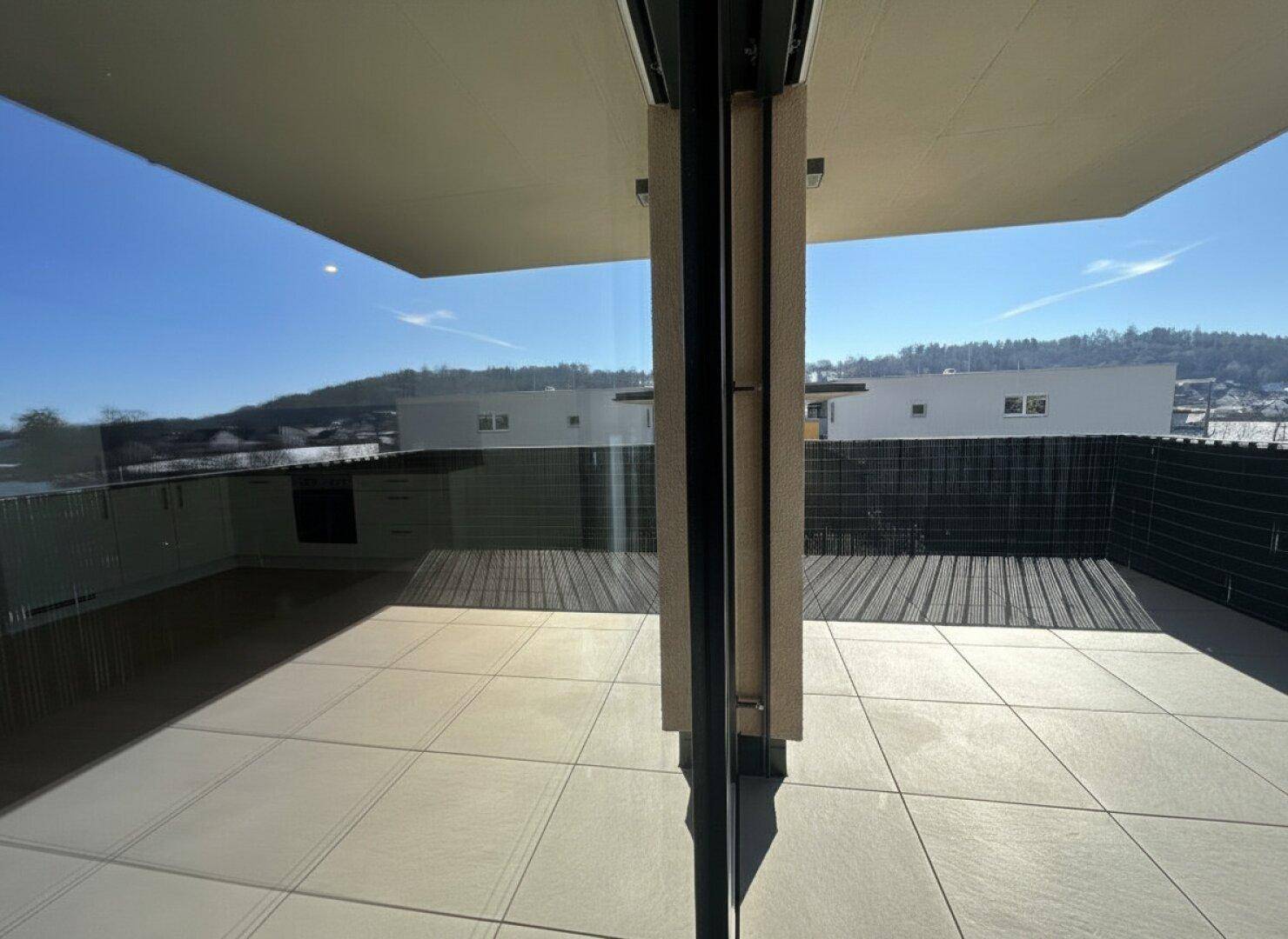 Terrasse mit Fliesenboden und weitem Blick auf die hügelige Landschaft unter blauem Himmel.