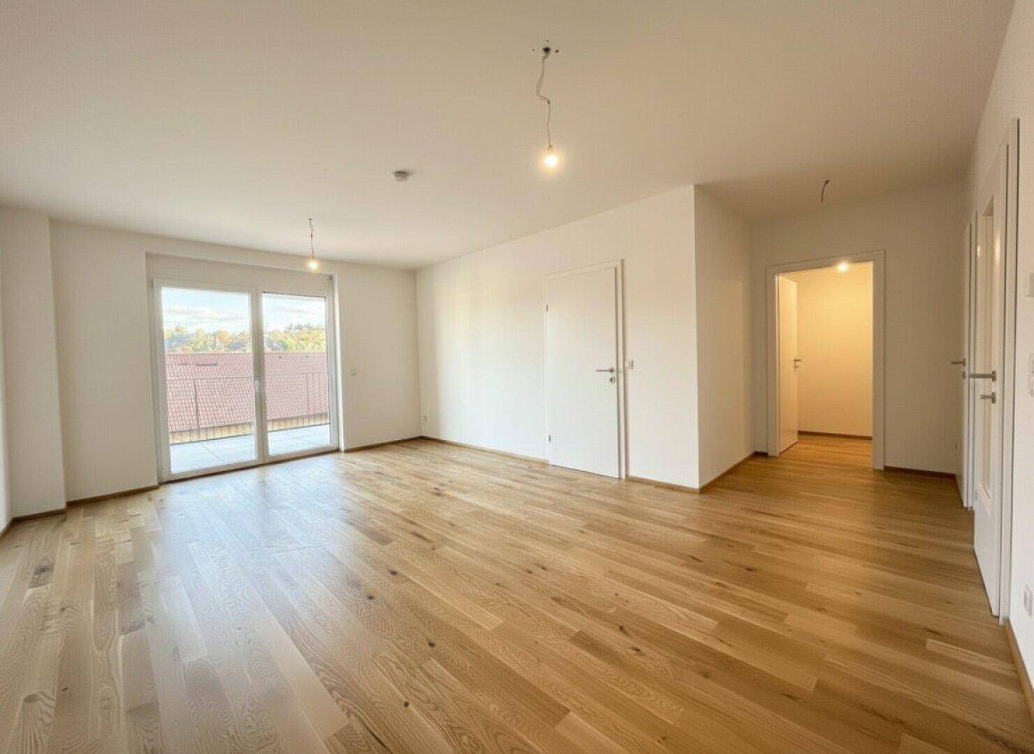Helles, leeres Zimmer mit Holzboden und Balkonzugang, bietet vielseitige Nutzungsmöglichkeiten.