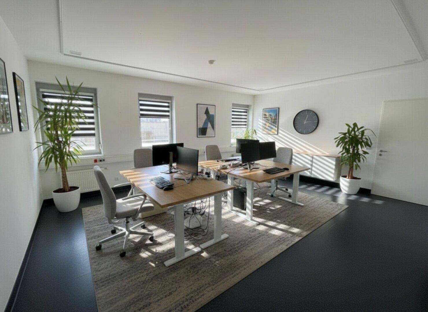 Modernes Büro mit mehreren Arbeitsplätzen, dunklem Vinylboden und Jalousien an den Fenstern für flexible Lichtregulierung.