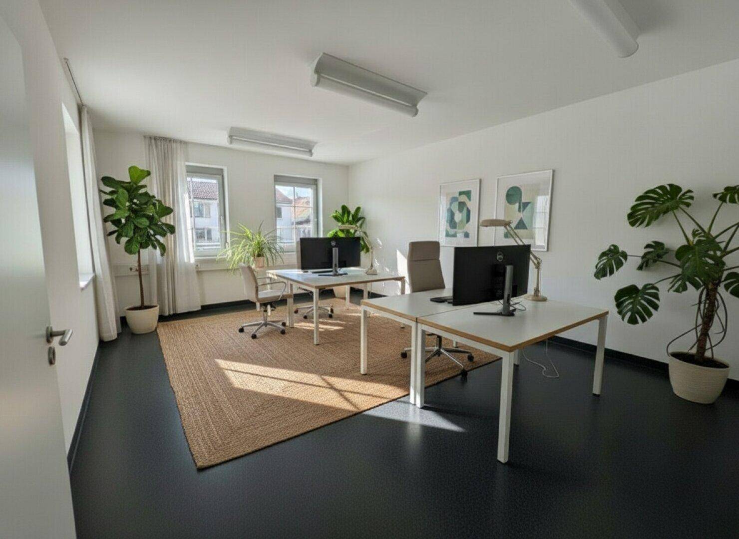 Geräumiges Büro mit modernen Arbeitsplätzen, dunklem Boden und einem großen Teppich, der eine gemütliche Atmosphäre schafft.