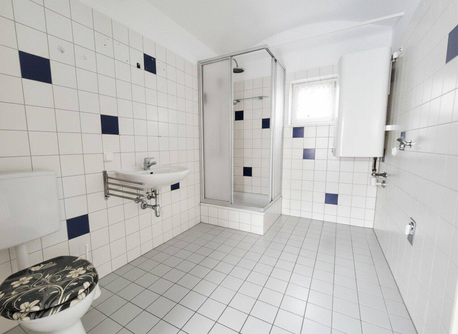 Geräumiges Badezimmer mit weißen Fliesen, blauen Akzenten und einer praktischen Duschkabine.
