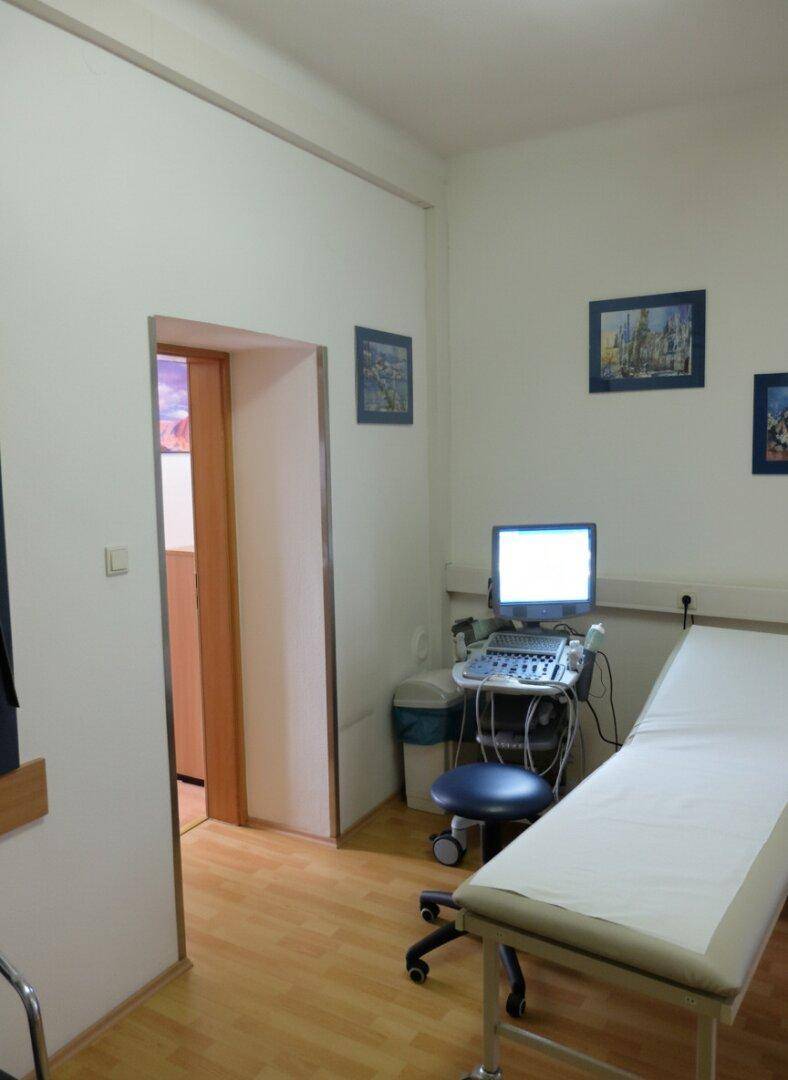 Praxisraum mit Untersuchungsliege, medizinischem Gerät und Holzboden.