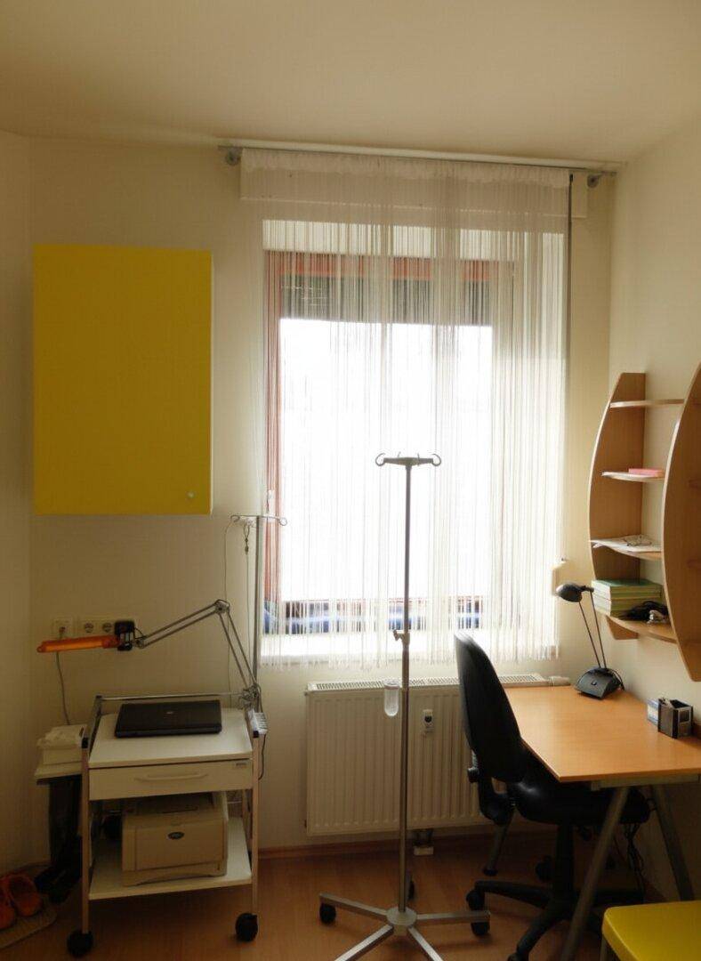 Funktional eingerichtetes Büro mit einem Fenster, Schreibtisch und medizinischem Ständer.