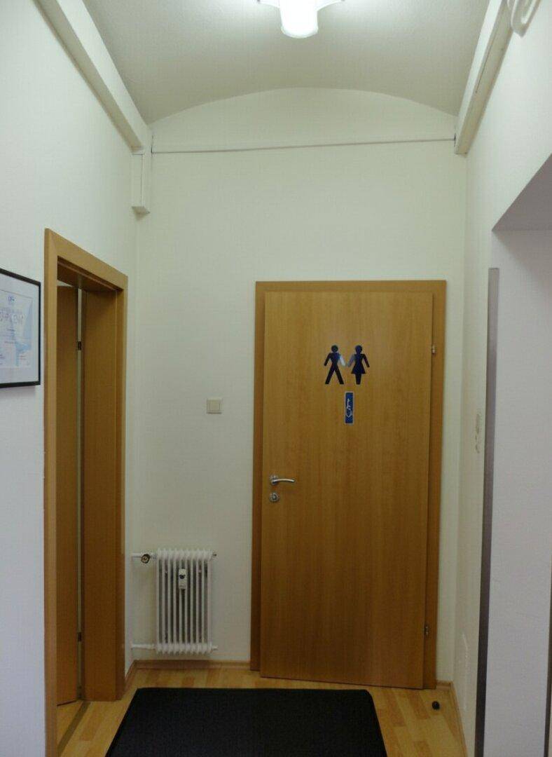 Flur mit gewölbter Decke und einer Tür, die zu den Toiletten führt.