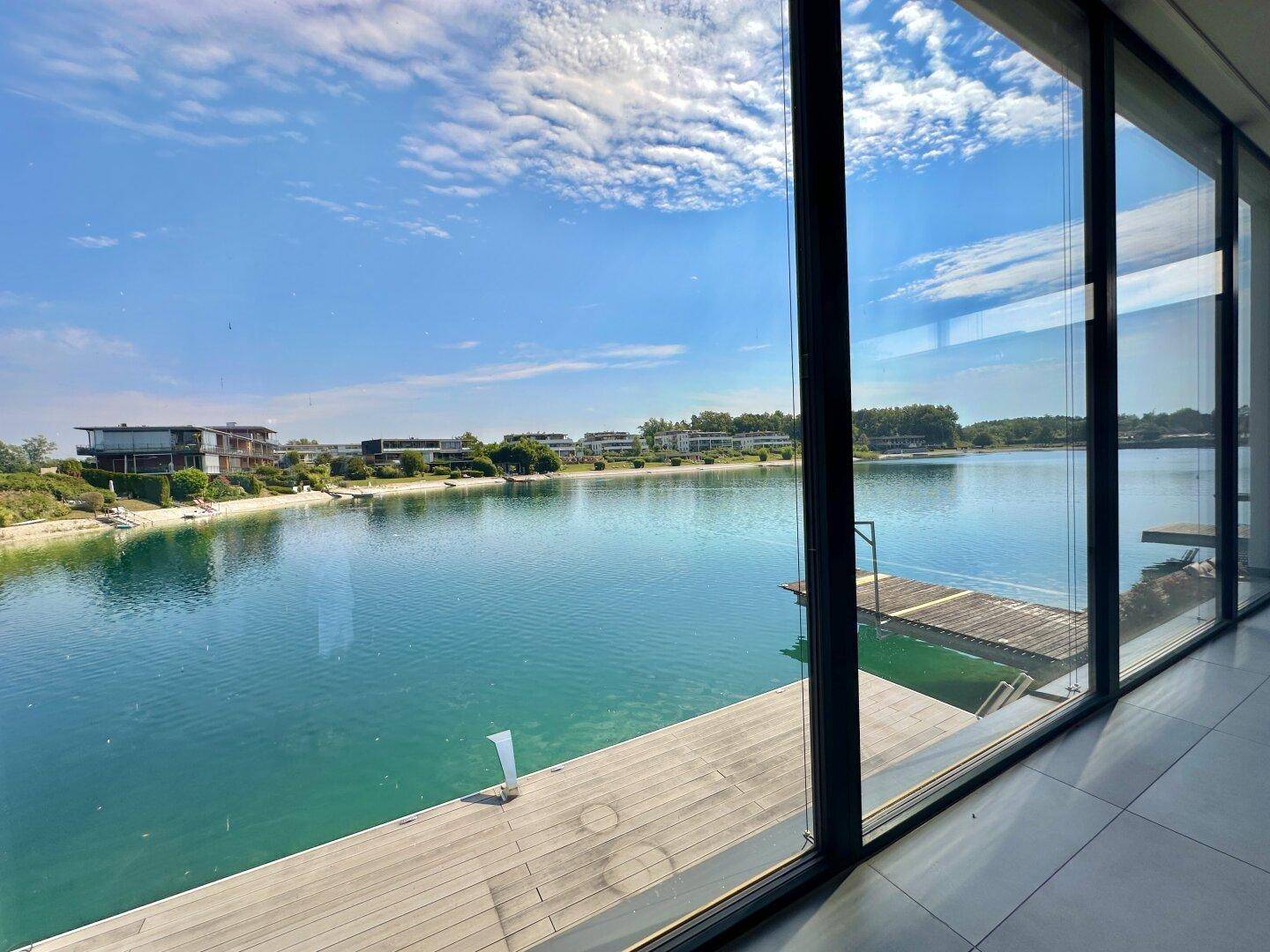 Panoramablick auf den See durch raumhohe Fenster von einem Innenraum.