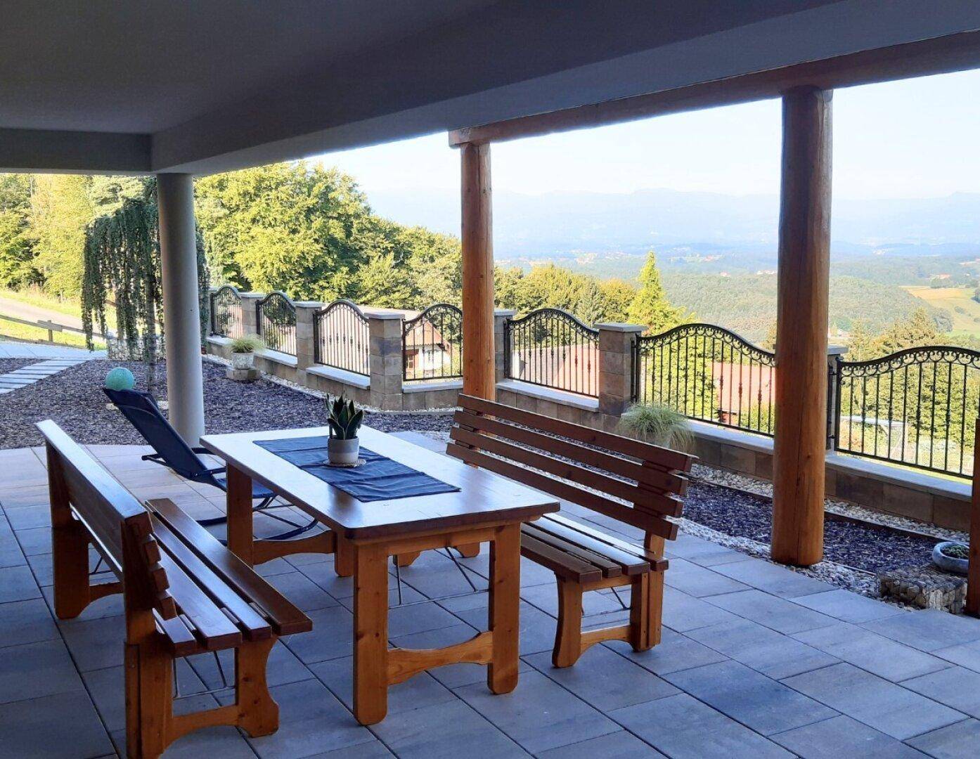 Überdachte Terrasse mit Holztisch und Bänken, bietet einen weiten Blick auf die grüne Landschaft.