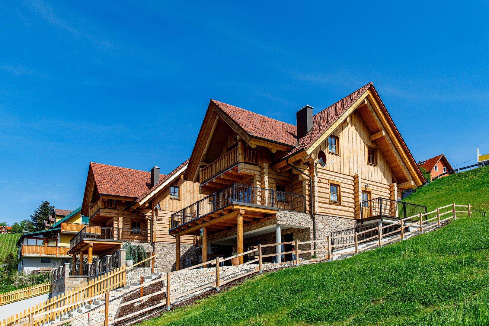 Attraktive Holzhäuser im Chalet-Stil auf einem grünen Hügel mit traditionellen Dächern.