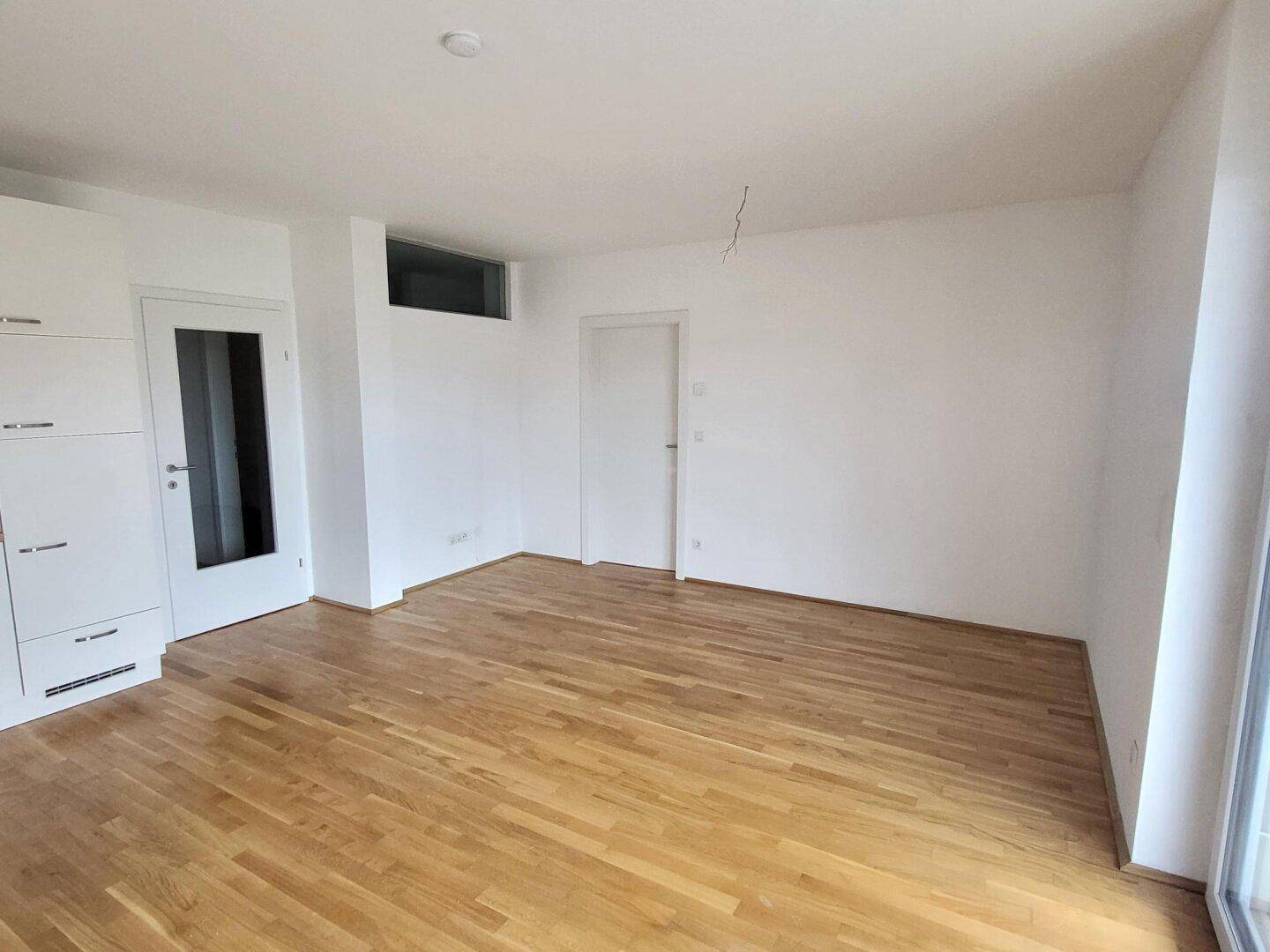 Leerer Wohnbereich mit hellem Parkettboden und weiß gestrichenen Wänden, bereit zur Einrichtung.