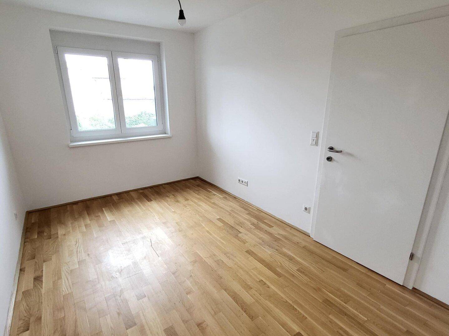 Unmöbliertes Schlafzimmer mit Parkettboden und einem Fenster, das für natürliches Licht sorgt.
