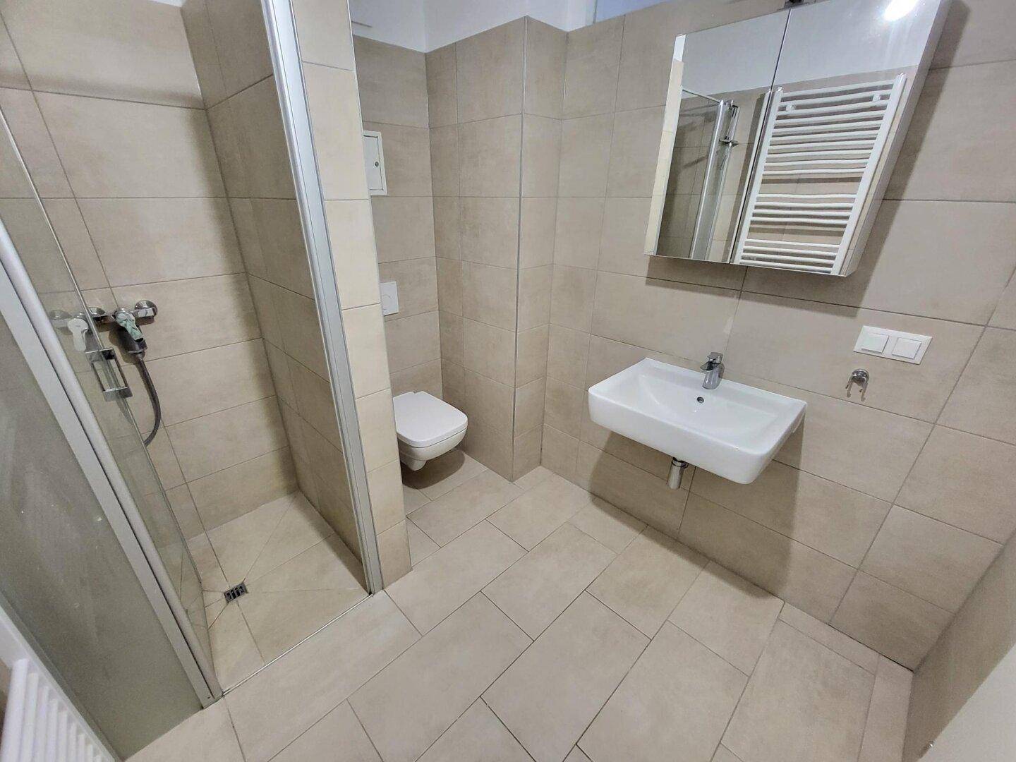 Modernes Badezimmer mit Duschkabine, wandhängendem WC, Waschbecken und hellen Fliesen.