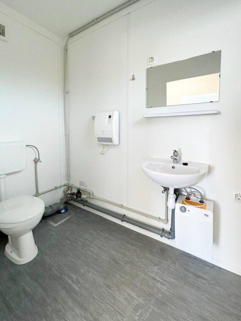 Modernes WC mit Waschbecken, Spiegel und Vinylboden, sauber und funktional eingerichtet.