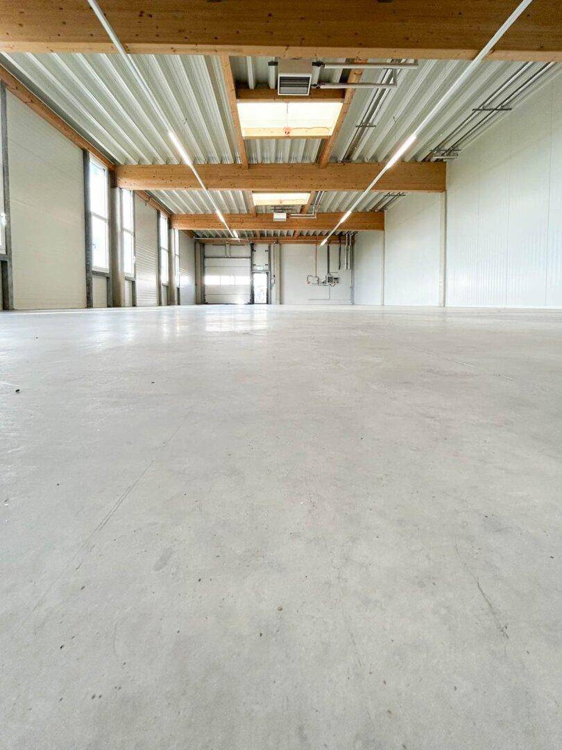 Große, leere Lagerhalle mit hohen Decken, Holzbalken und Betonboden, ideal für gewerbliche Nutzung.