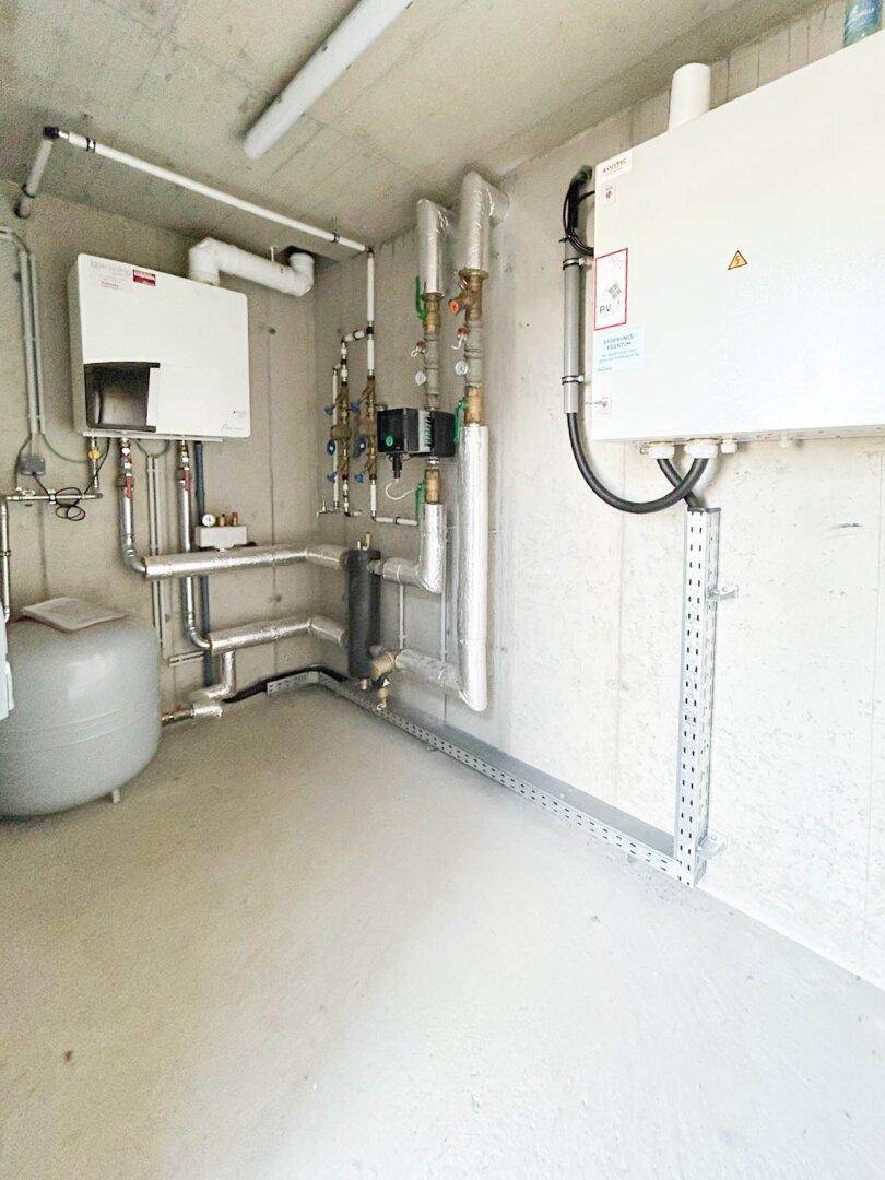 Technikraum mit Heizungsanlage, Warmwasserspeicher und zahlreichen Rohren, ordentlich installiert.