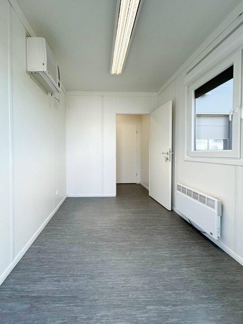 Helles Büro in einem Anbau mit Vinylboden, Klimaanlage und Heizkörper, bereit zur Einrichtung.