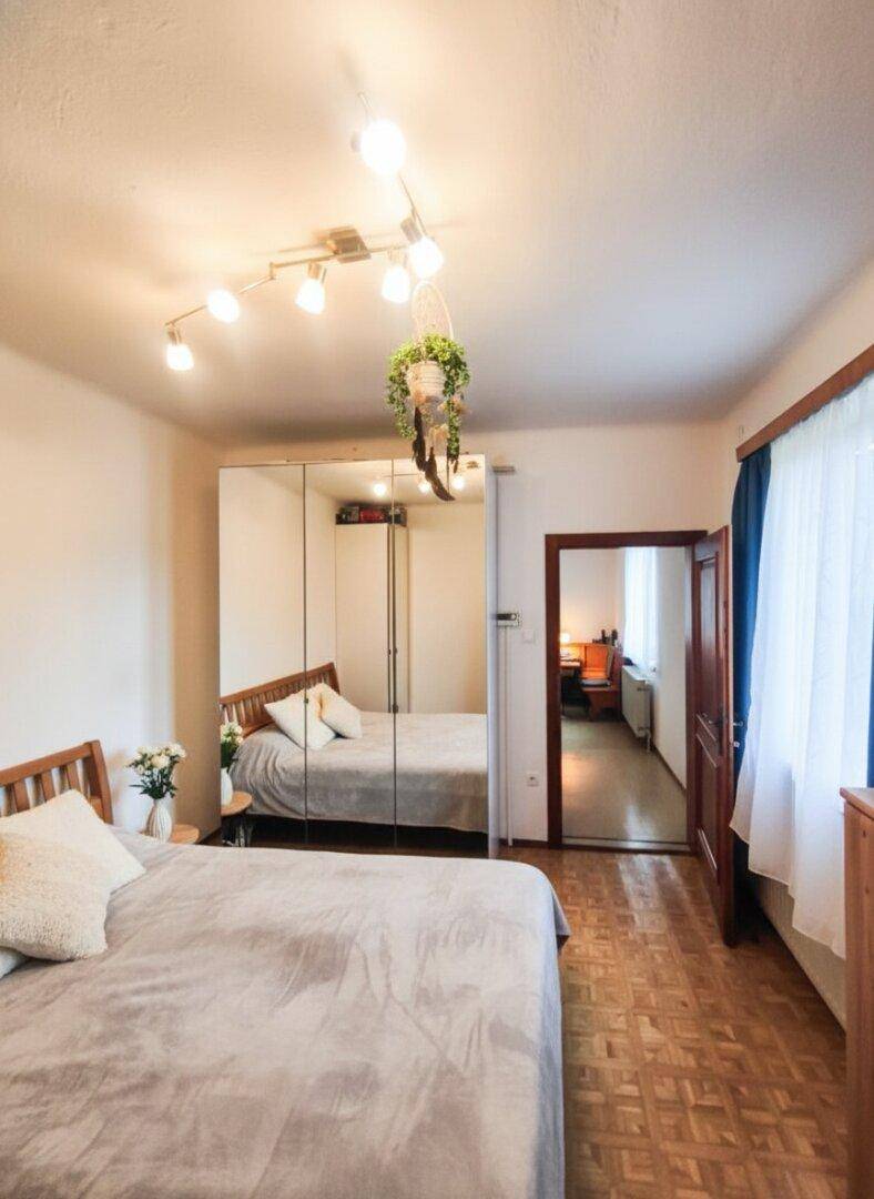 Schlafzimmer mit Parkettboden, Spiegelschränken und Zugang zu einem weiteren Raum.