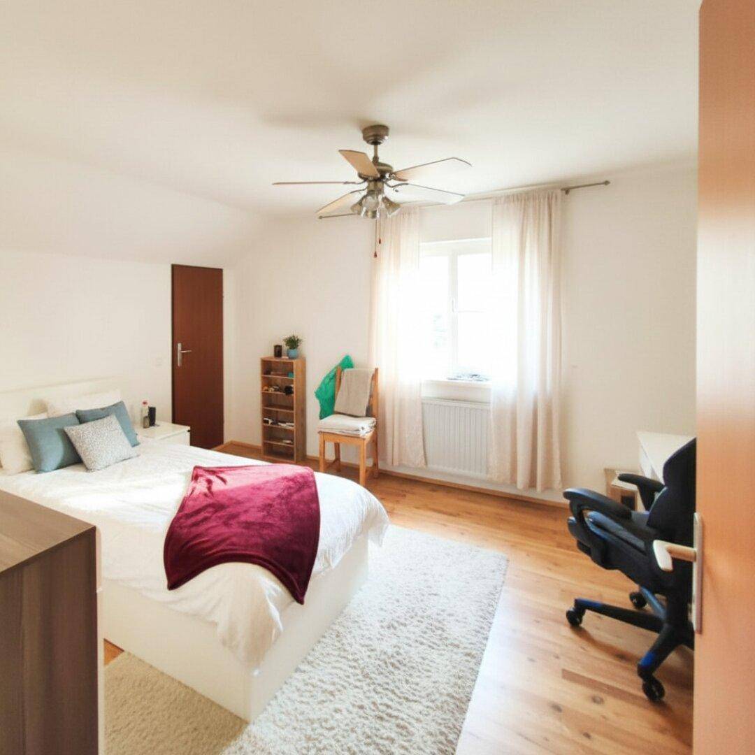 Helles Schlafzimmer mit Holzboden, Deckenventilator und Schreibtischbereich am Fenster.