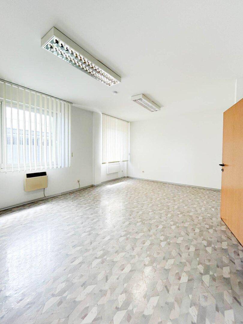Leerer Büroraum mit weißen Wänden, gemustertem Boden und Fensterjalousien, bereit zur Einrichtung.